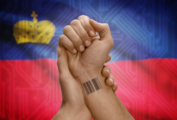 Barcode ID number on wrist of dark skinned person and national flag on background - Liechtenstein
