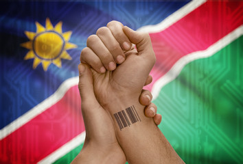 Barcode ID number on wrist of dark skinned person and national flag on background - Namibia