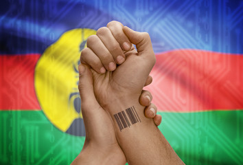 Barcode ID number on wrist of dark skinned person and national flag on background - New Caledonia