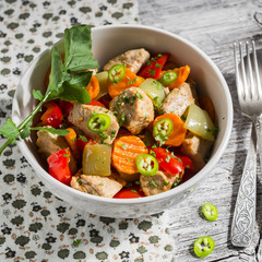 meat stew with vegetables - carrots, onions and sweet peppers in a white bowl on a light wooden background