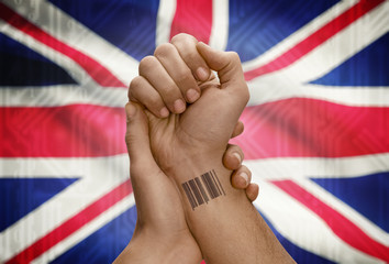Barcode ID number on wrist of dark skinned person and national flag on background - United Kingdom
