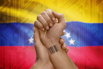 Barcode ID number on wrist of dark skinned person and national flag on background - Venezuela