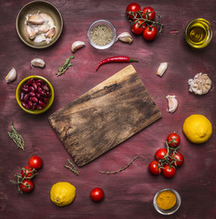 Ingredients for cooking vegetarian food tomatoes on a branch, lemon, olive oil, red hot pepper, herbs, cutting board , frame, with text area on wooden rustic background top view
