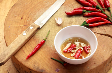 Fish sauce in white bowl,knife,wooden cutting board,chili on tab