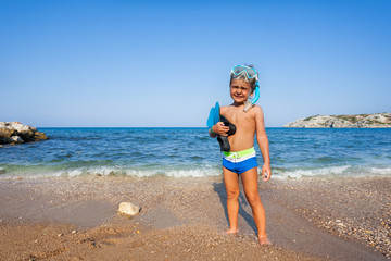 Boy with mask and paddles stands on the seashore