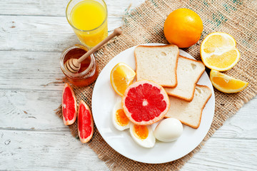 
Healthy diet breakfast, boiled eggs with white toast, fresh grapefruit and oranges , honey and orange juice on a wooden background