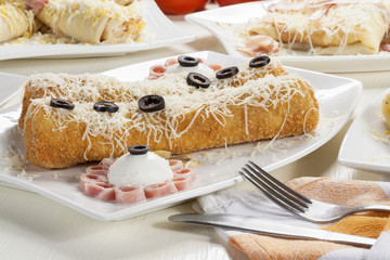 Two breaded pancakes with savory filling served on a white plate with ham, sour cream, cheese and olives.