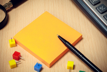 black pen,orange paper note,colorful peg,magnifier,calculator on