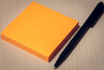 black pen,orange paper on wood table background.