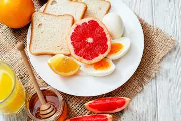 
Healthy diet breakfast, boiled eggs with white toast, fresh grapefruit and oranges , honey and orange juice on a wooden background