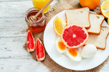 
Healthy diet breakfast, boiled eggs with white toast, fresh grapefruit and oranges , honey and orange juice on a wooden background