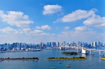 Naklejka premium Daytime waterfront Tokyo skyline with modern skyscrapers, Rainbow bridge on sunny cloudy day