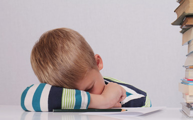 Naklejka premium Cute tired school boy sleeping while doing homework