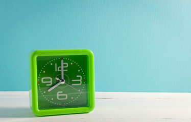 beautiful green clock on white table and green background.