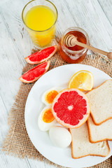 Fototapeta na wymiar Healthy diet breakfast, boiled eggs with white toast, fresh grapefruit and oranges , honey and orange juice on a wooden background