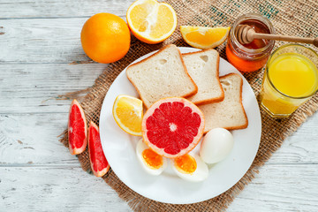
Healthy diet breakfast, boiled eggs with white toast, fresh grapefruit and oranges , honey and orange juice on a wooden background