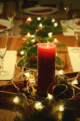 Christmas table decoration with red candle and fir tree twigs lying on the table with electric garland lights on