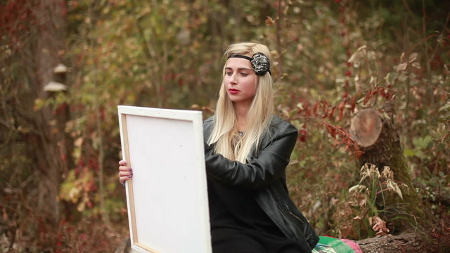 Attractive young woman sitting on log and drawing picture