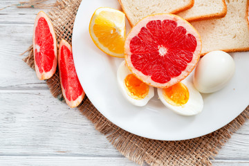 
Healthy diet breakfast, boiled eggs with white toast, fresh grapefruit and oranges , honey and orange juice on a wooden background