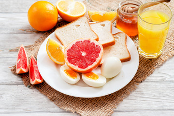
Healthy diet breakfast, boiled eggs with white toast, fresh grapefruit and oranges , honey and orange juice on a wooden background