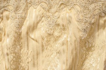 Yellow gold textile pattern as a background. Close up on crumpled sparkly gold material with lace on fabric.