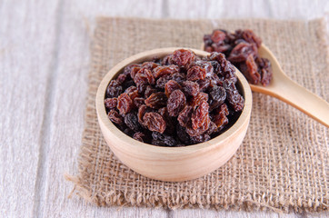 dry raisins in wooden bowl and spoon on white wooden table