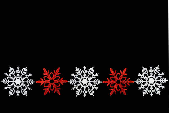 A Row Of Fake Plastic Snowflake Ornaments On A Black Background.