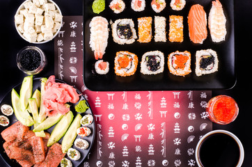 Sushi set, soy sauce, ginger, wasabi, black and red roe, avocado, salmon, cheese on black background with Japanese characters