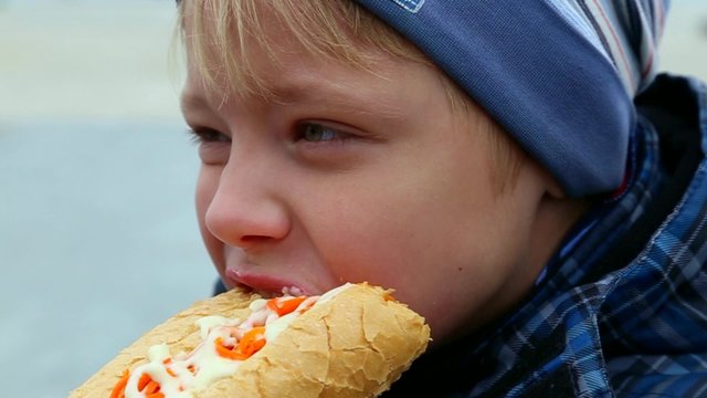 Closeup of child eating hotdog outside in city street. Real time video footage.