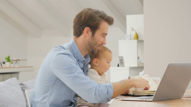 Man working form home on laptop, baby on lap
