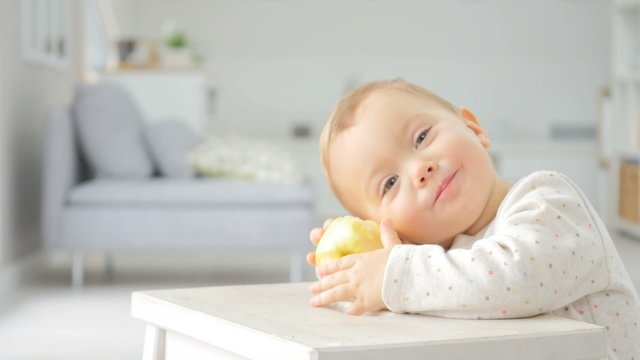 Cute 15-month-old baby girl eating an apple