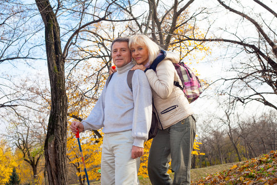     Mature man and woman hikers stand embracing in autumn forest 