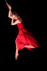 Woman gymnast in red dress on rope on black background