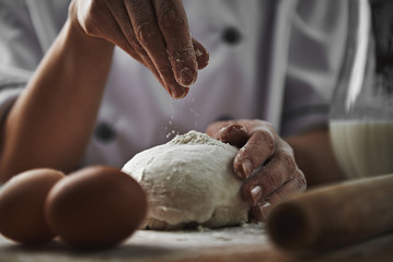 Female in chef uniform adding flour to dough preparing pizza in the kitchen. Cookery and healthy nourishment concept.  - obrazy, fototapety, plakaty