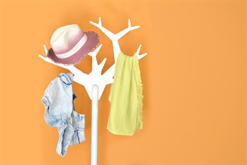 Clothes hanger stand with hat, jeans and scarf on an orange background