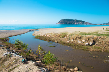 Fototapeta na wymiar Confluence of the mountain river in the sea on beach in Alanya T