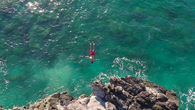 Cliff Jumping into Ocean. Aerial View Slow Motion. Young Man Jumps off Cliff Into Blue Ocean. Summer Extreme Sports Outdoor Lifestyle. 