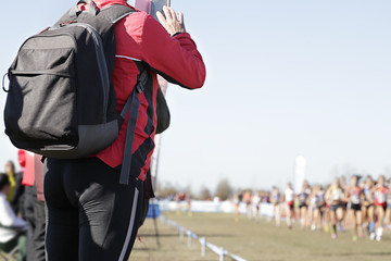 Fototapeta premium Woman taking a picture with her phone of some runners who are running a popular race