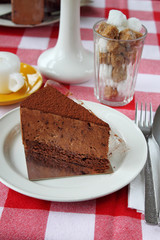 slice of chocolate cake on a white plate decorated with white vase of flowers