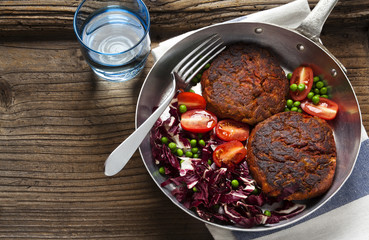 two Vegan Burgers and salad in a frying pan.