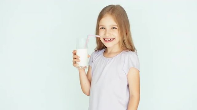 Happy child drinking milk. Girl with beautiful blond hair on a white background. Thumb up. Ok