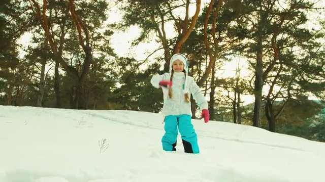 Happy child in winter forest. Girl looking at the camera and waving hand