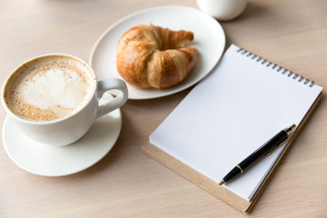 coffee , notebook and croissant on a wooden table