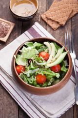 Salad with lettuce, tomatoes, flax seeds and avocado in a wooden bowl. Top view.