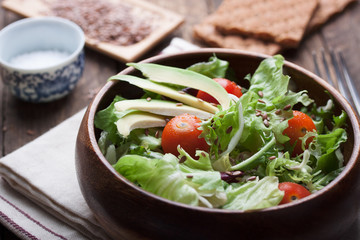 Salad with lettuce, tomatoes, flax seeds and avocado in a wooden bowl. Closeup.