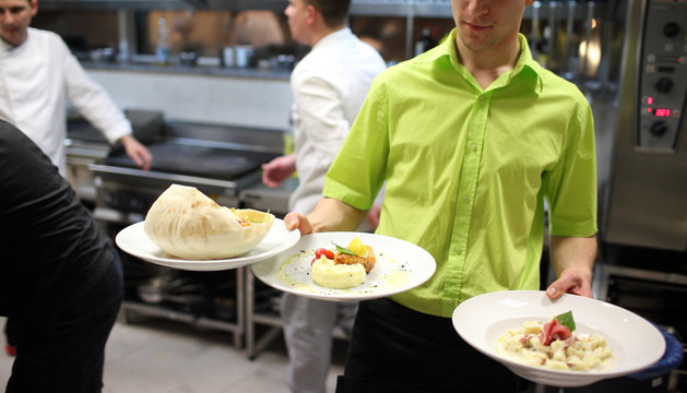 Waiter carrying a plate with salad dish . Cook in the background