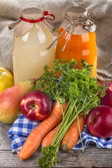 .Different bottles of juice with ripe fruits and vegetables on rustic table and in front of the linen background..