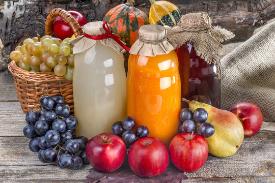 Different bottles of fresh juice with ripe fruits and vegetables on rustic table and in front of wood.