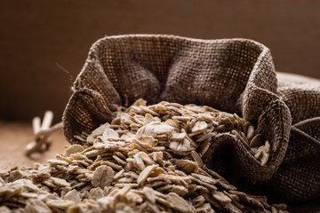 Obraz premium oat flakes cereal in burlap sack on wooden table.