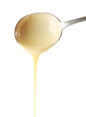 Condensed milk pouring from a spoon, isolated on white